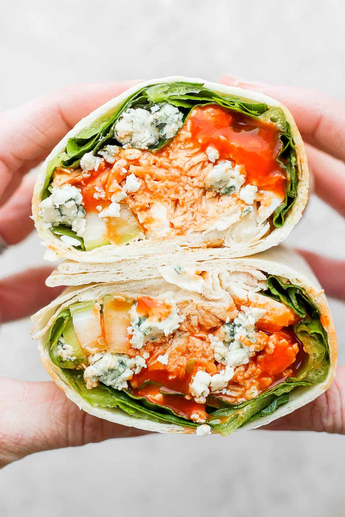 Two hands holding a buffalo chicken wrap cut in half.