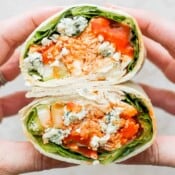 Someone holding two sides of a buffalo chicken wrap, showing the inside.