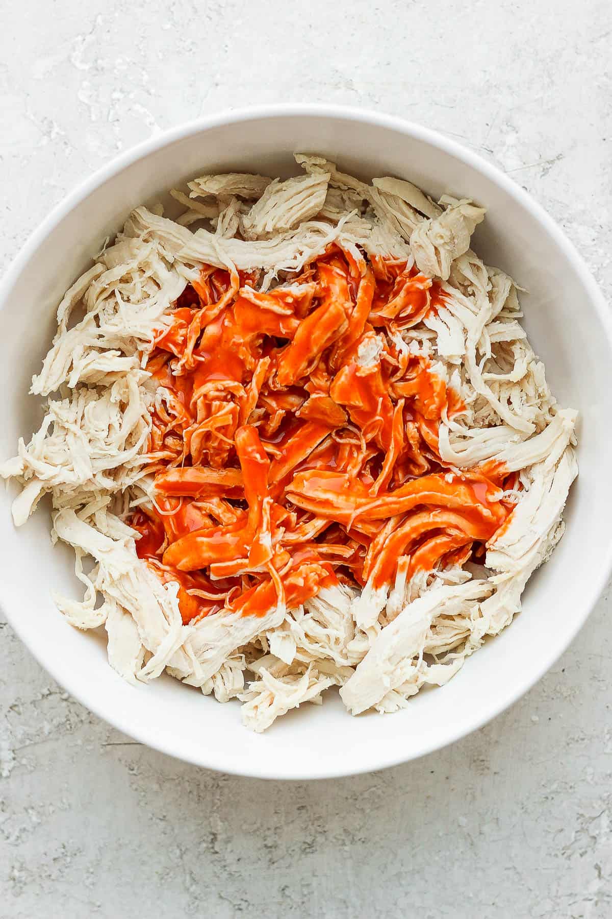 A bowl of shredded chicken with buffalo sauce.