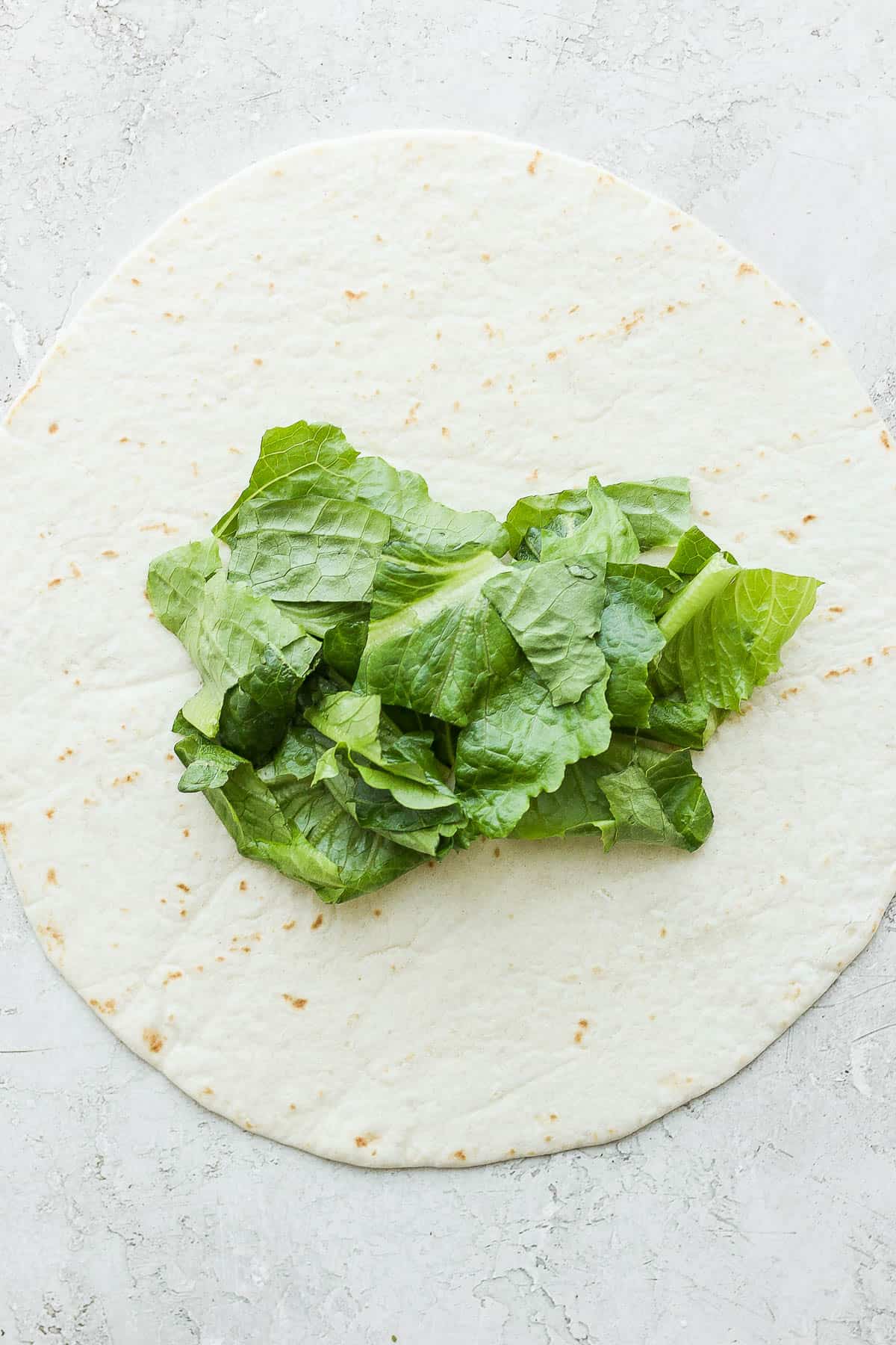A burrito-sized tortilla with lettuce in the middle to begin the wrap.
