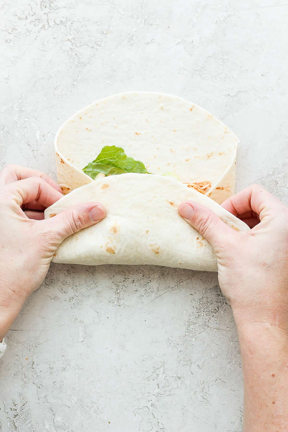 Two hands pulling up the bottom of the tortilla.
