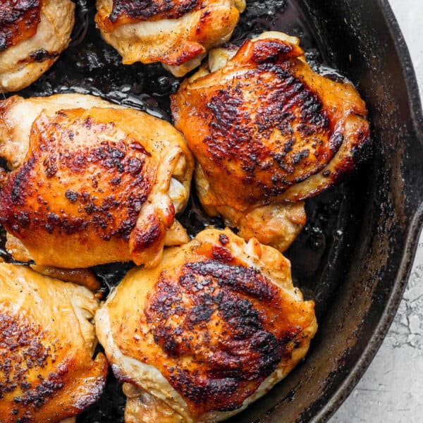 Cast iron skillet with cooked chicken thighs inside.