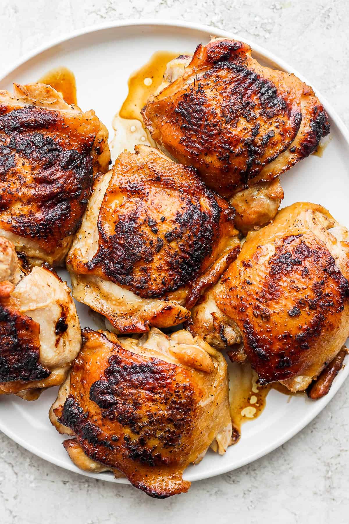 Six cast iron chicken thighs resting on a white plate after being cooked.