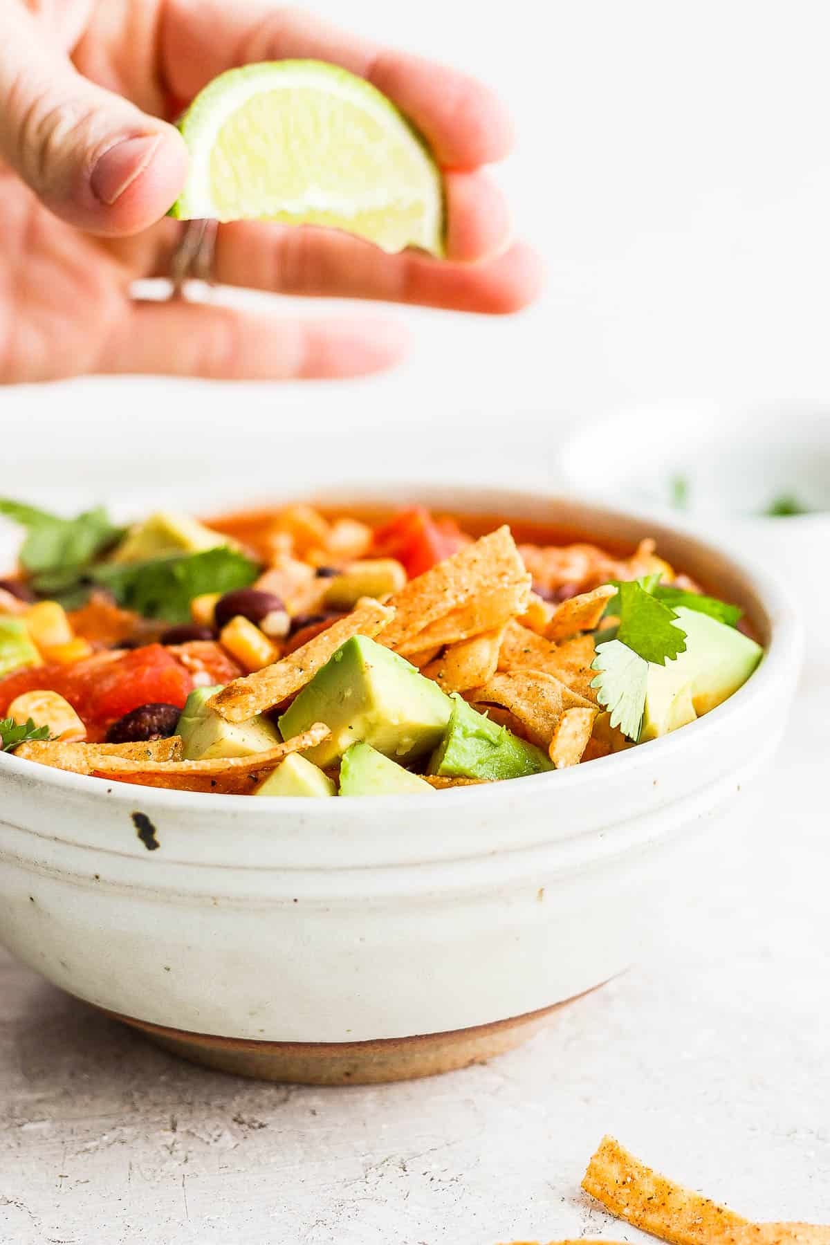 A lime wedge being squeezed over a bowl of chicken tortilla soup.