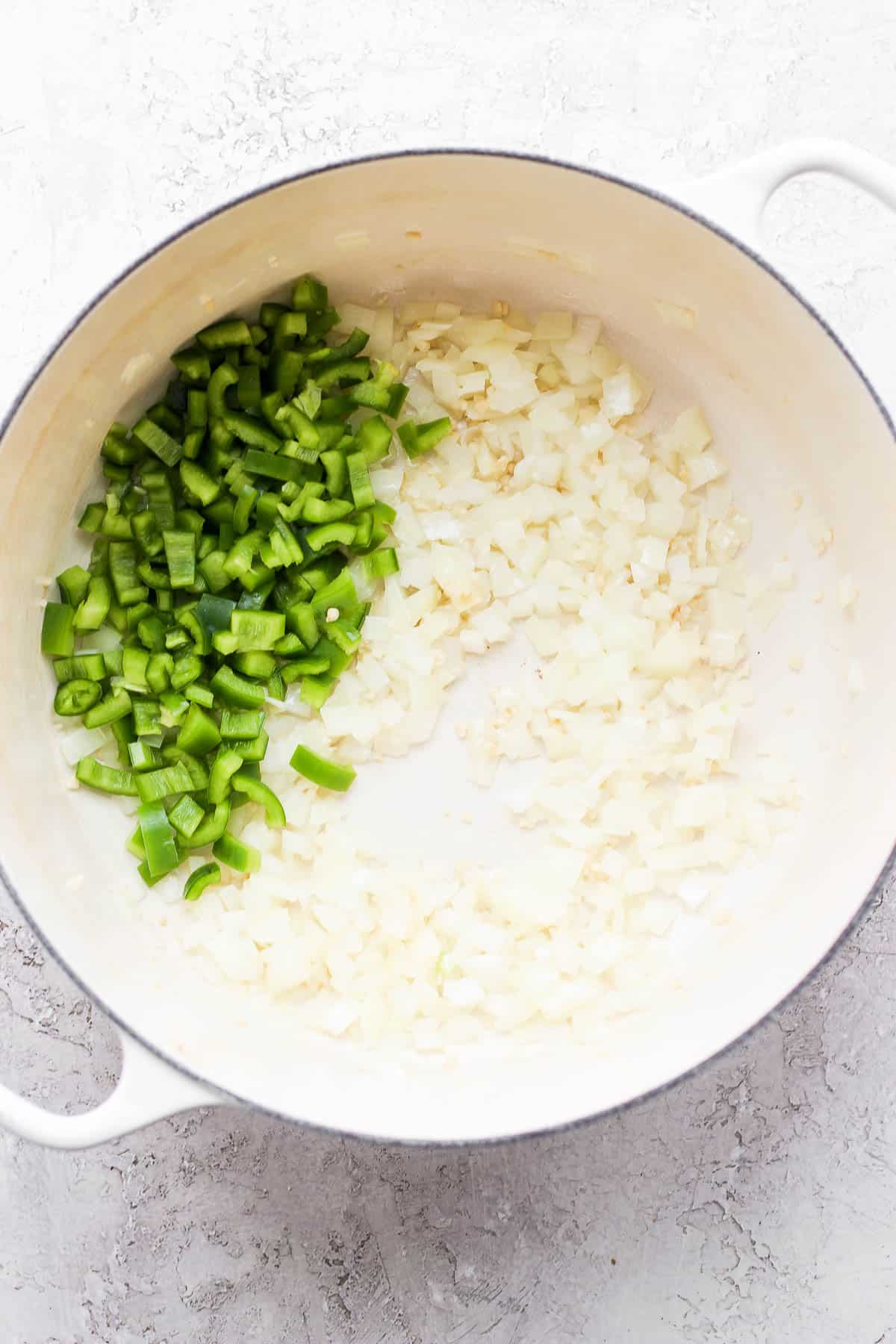 A dutch oven with olive oil, onion, garlic, and pepper.