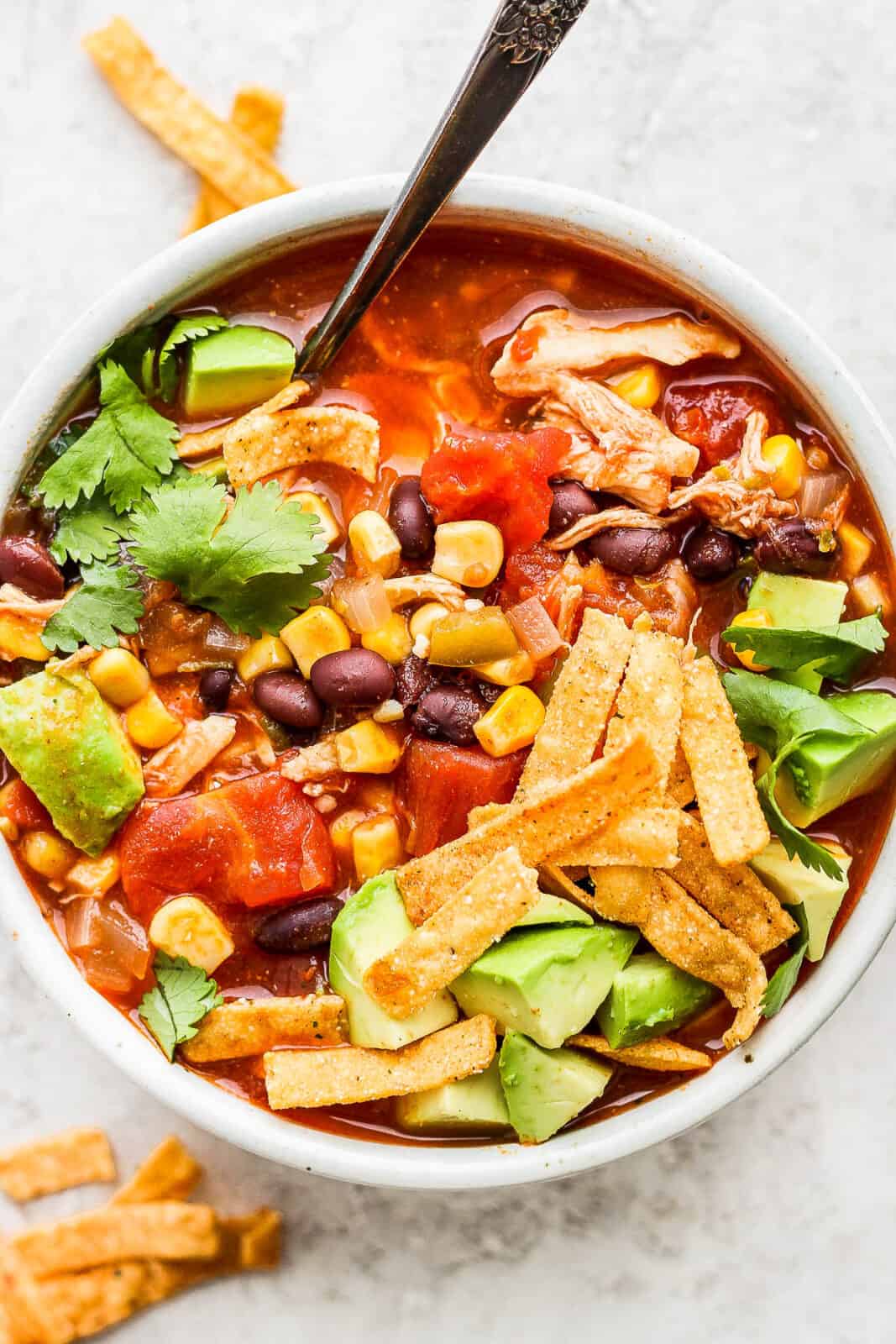 A bowl of chicken tortilla soup with a spoon.