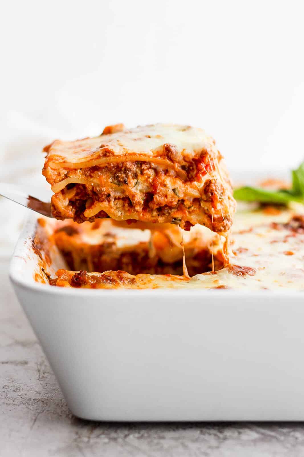 A small spatula lifting a piece of lasagna out of the pan.