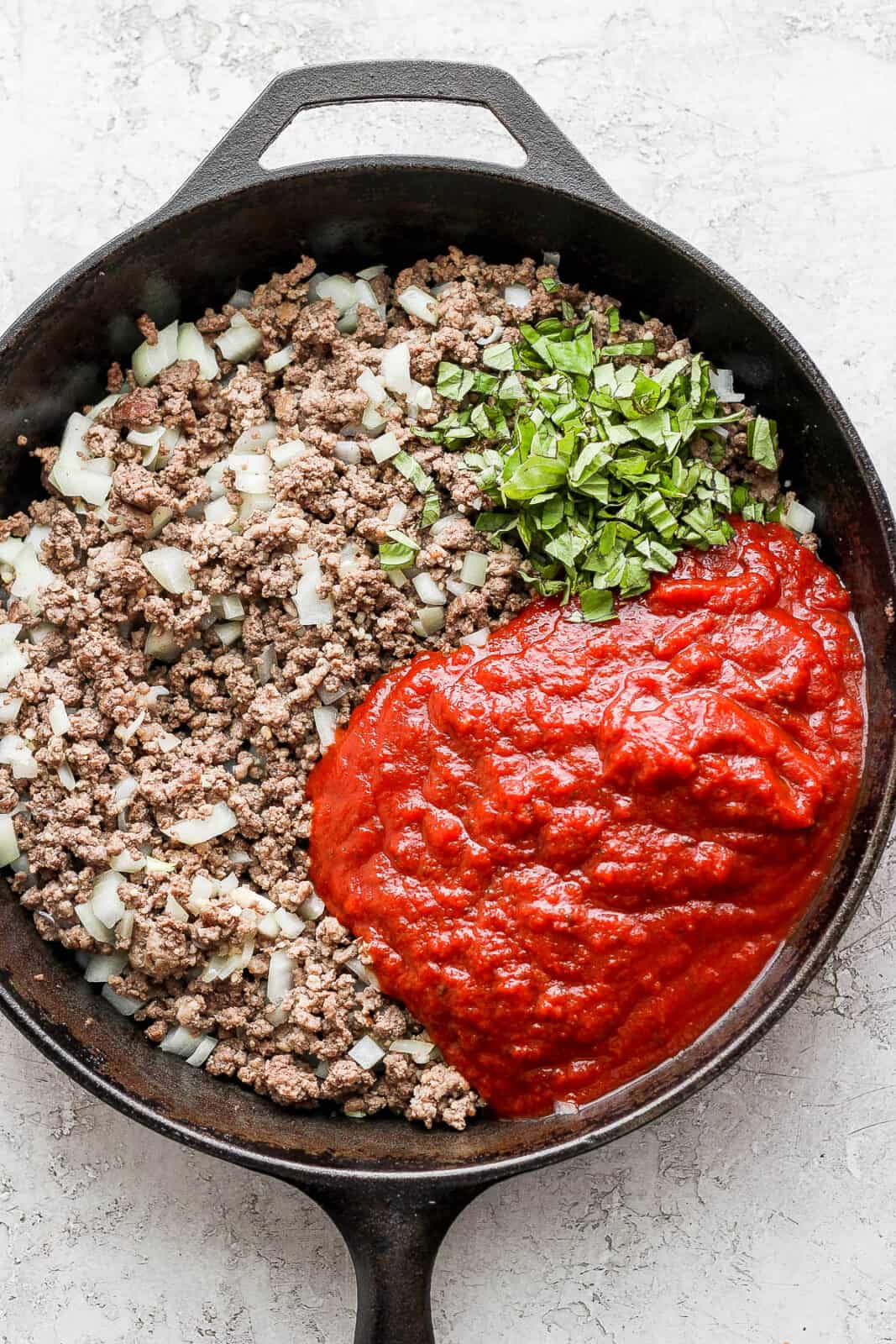 Browned meat in a skillet with basil and marinara sauce added.