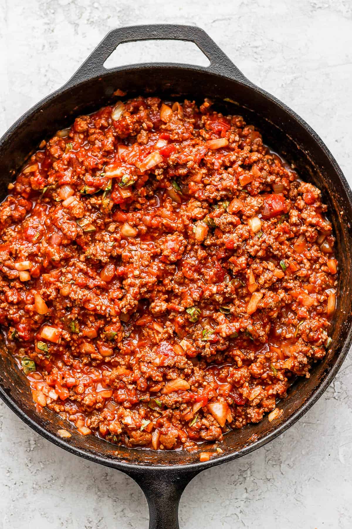 A cast iron skillet filled with a meat sauce.