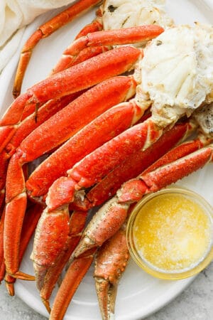 Grilled crab legs on a platter with little bowl of melted butter.