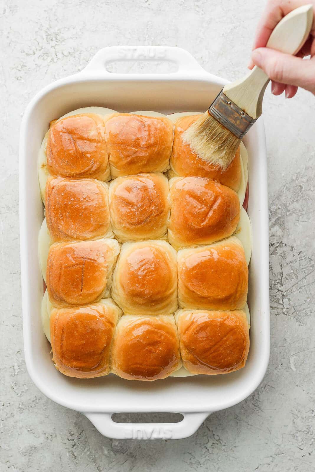 Melted butter being brushed on the top of the sliders.