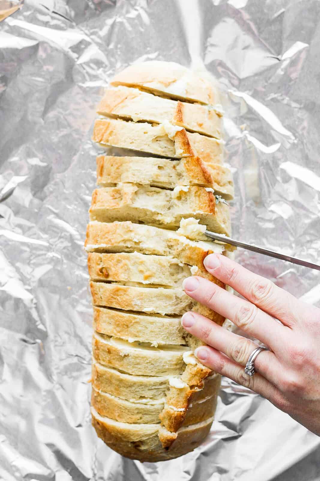 Garlic butter being spread between the bread slices.