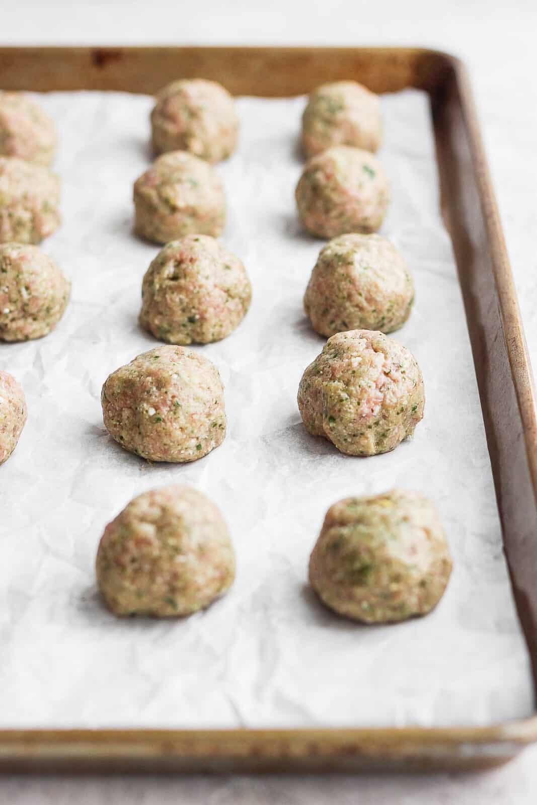 Raw meatballs lined up on parchment-lined baking sheet.