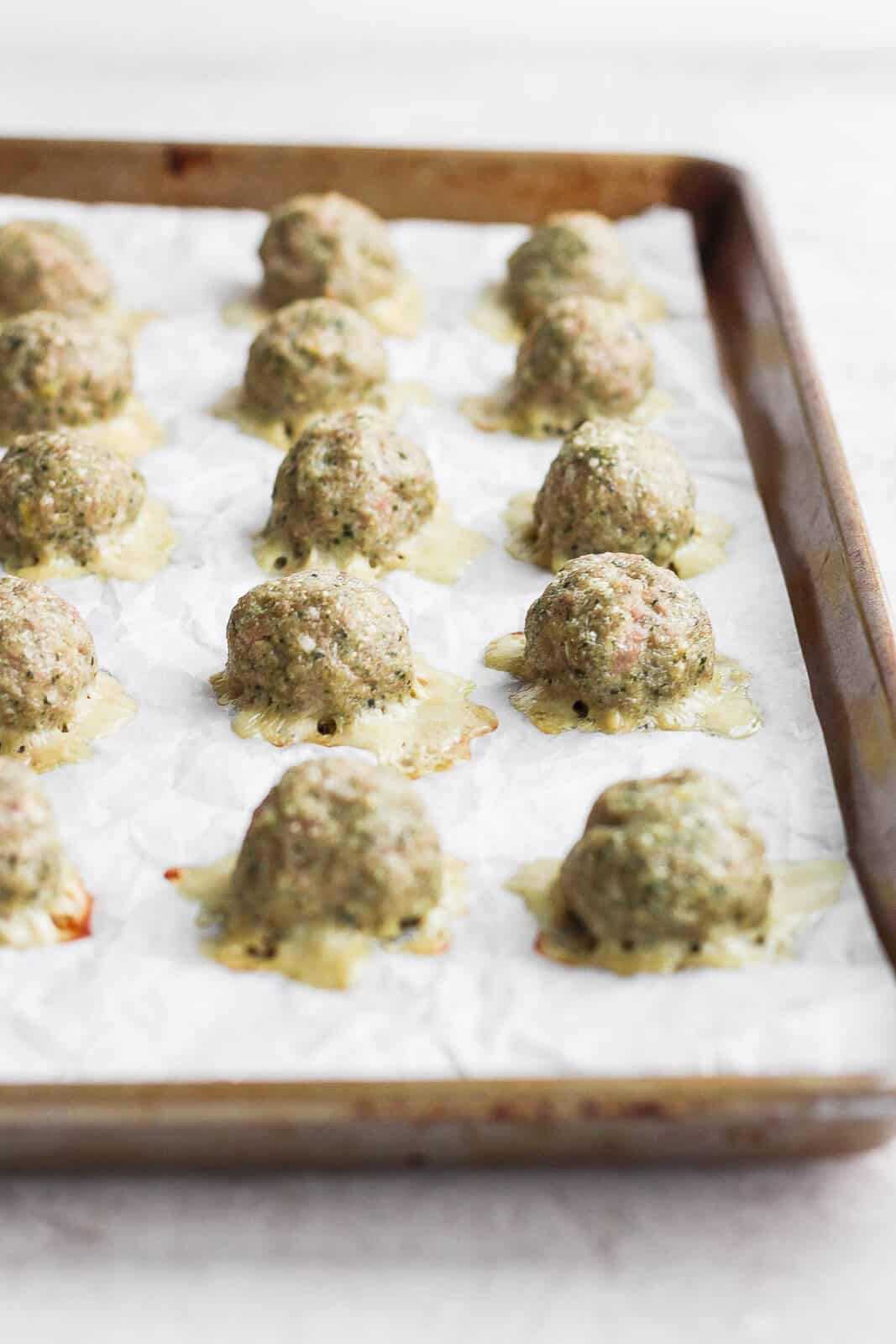 Cooked pesto meatballs on parchment-lined baking sheet.