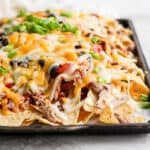 Side view of a sheet pan full of pulled pork nachos.