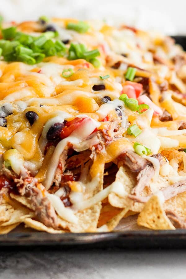 Side view of a sheet pan full of pulled pork nachos.