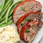 A plate of three slices of smoked meatloaf, smoked green beans and mashed potatoes.