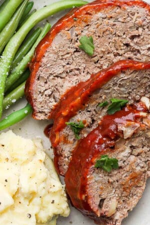 A plate of three slices of smoked meatloaf, smoked green beans and mashed potatoes.