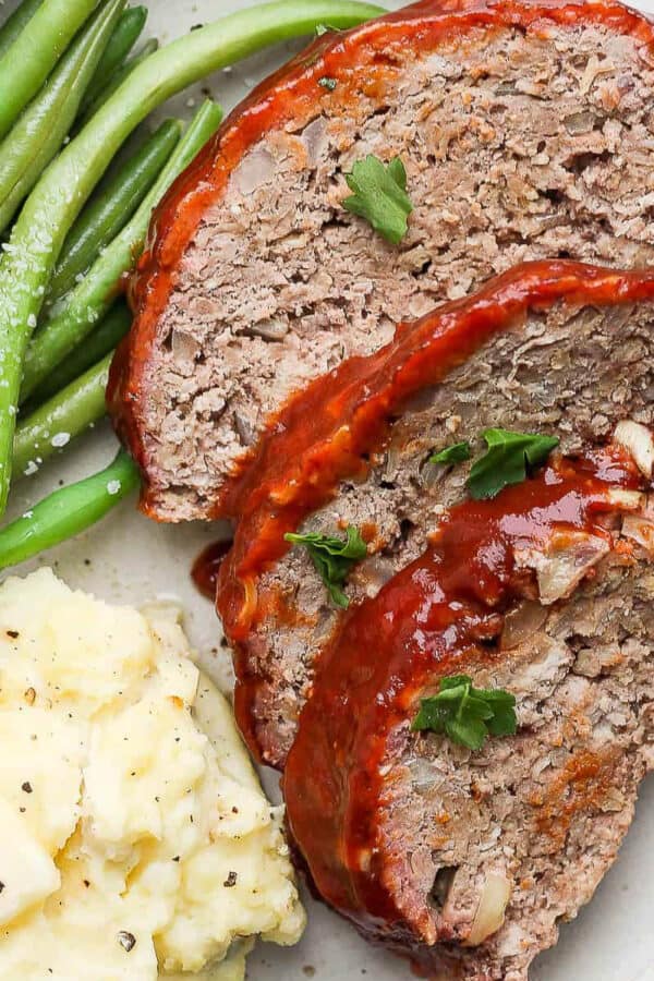 A plate of three slices of smoked meatloaf, smoked green beans and mashed potatoes.