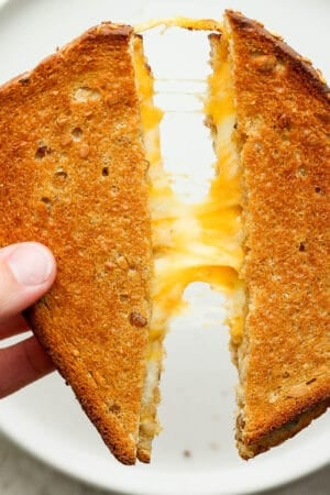 An air fryer grilled cheese cut in half and being pulled apart with cheese in the middle.