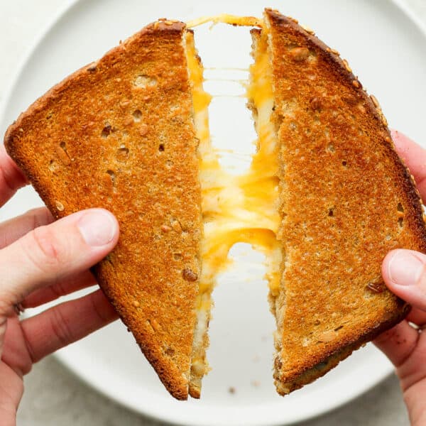 An air fryer grilled cheese cut in half and being pulled apart with cheese in the middle.