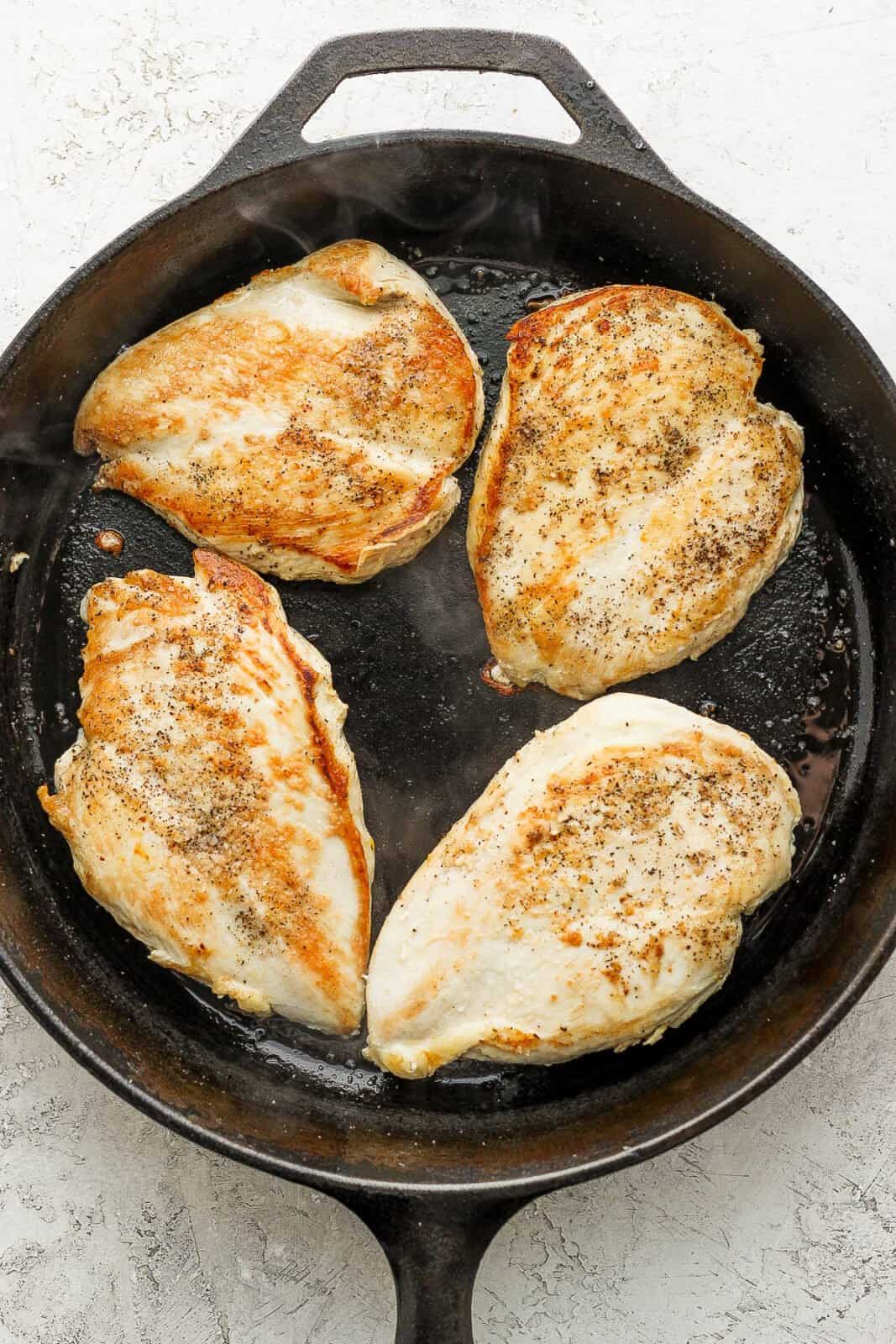 Cast iron skillet with 4 chicken breasts inside.