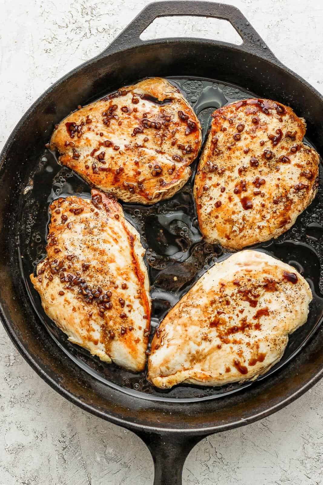 Four seared chicken breasts with balsamic reduction around them. 