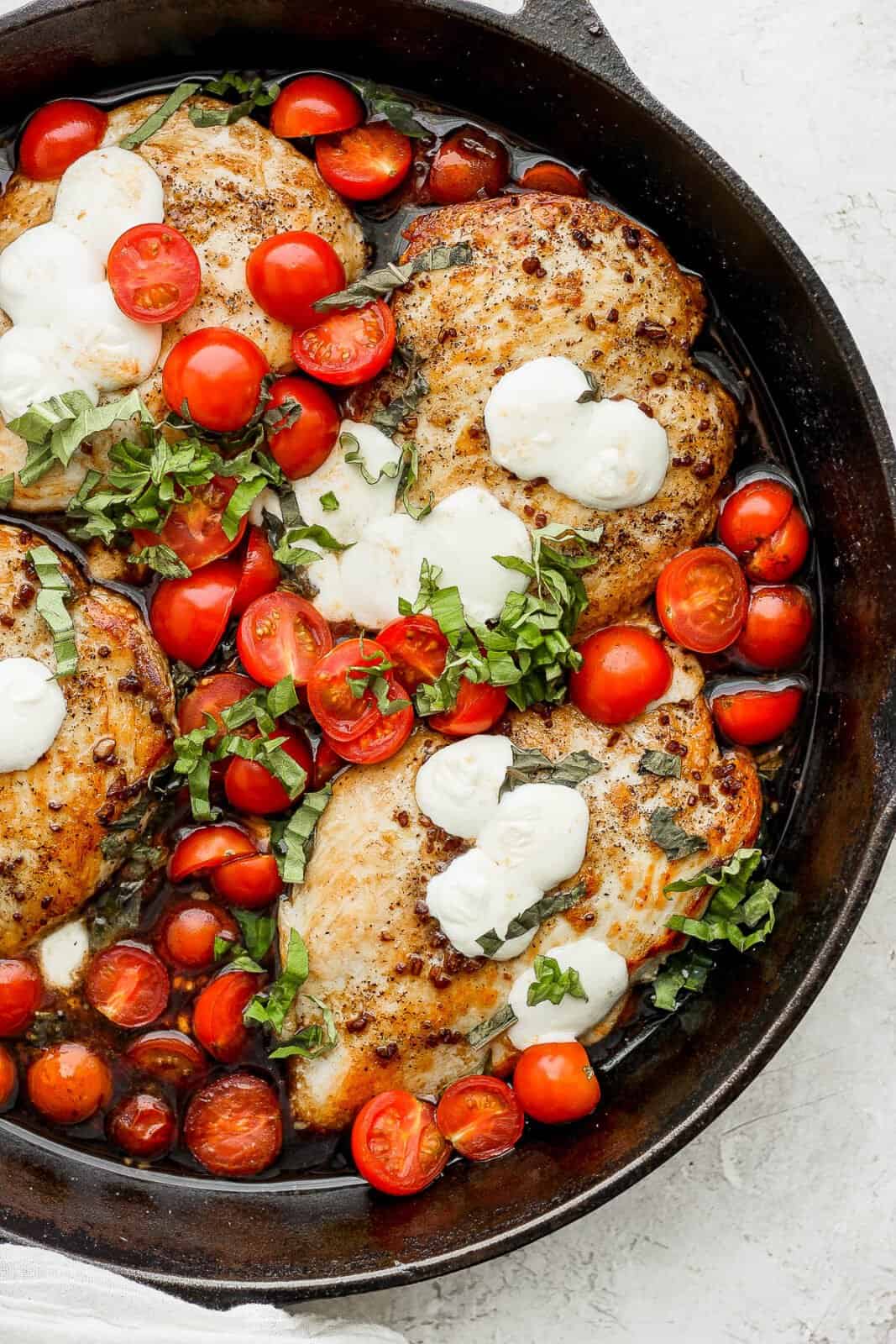 A large cast iron skillet filled with balsamic chicken with tomatoes and melted mozzarella. 