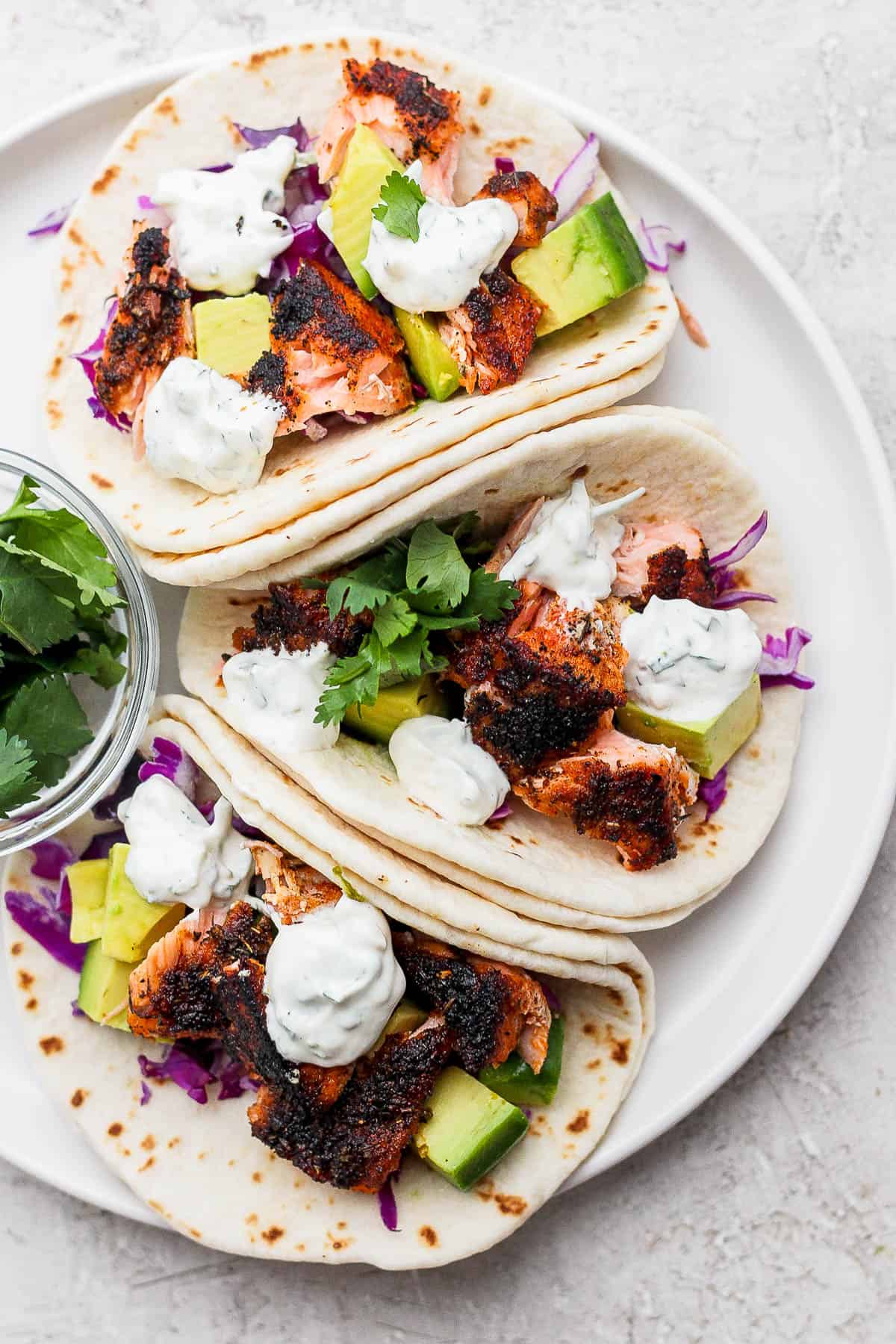 Three blackened salmon tacos with cilantro lime crema on a plate.