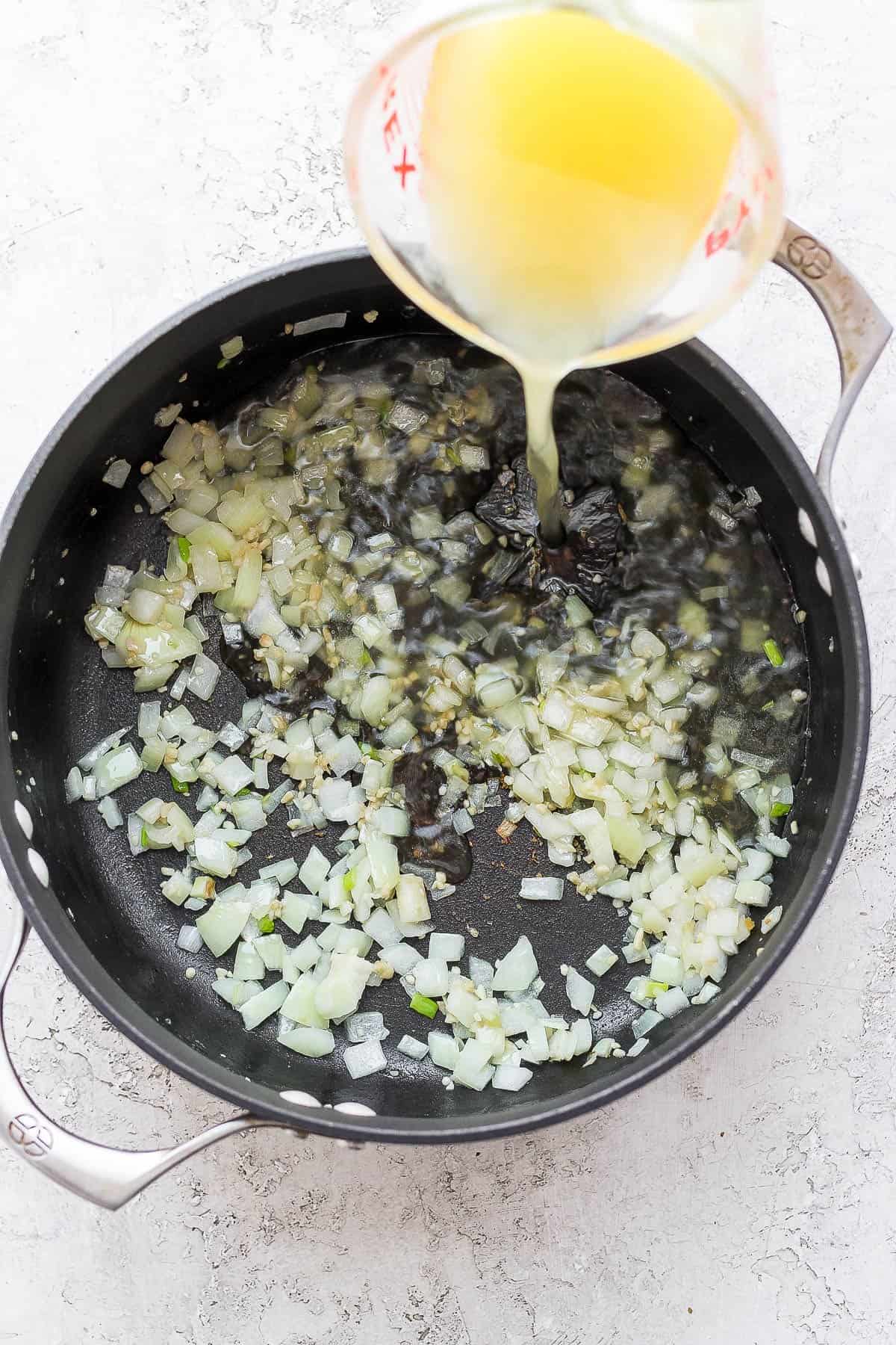 Garlic and onion being sautéed in a dutch oven with broth being added.