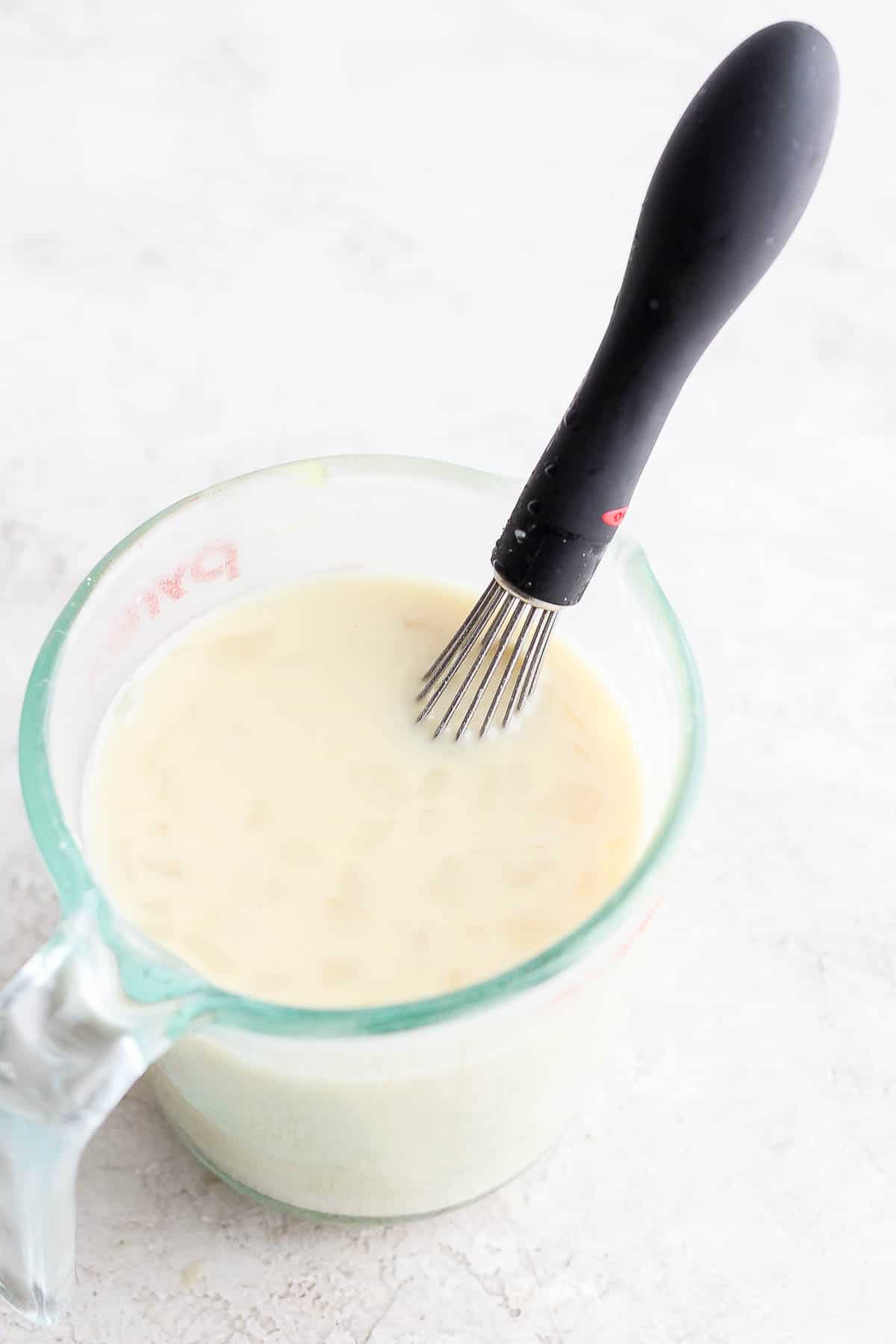 A broth and flour slurry mixed together with a whisk in a mixing cup.