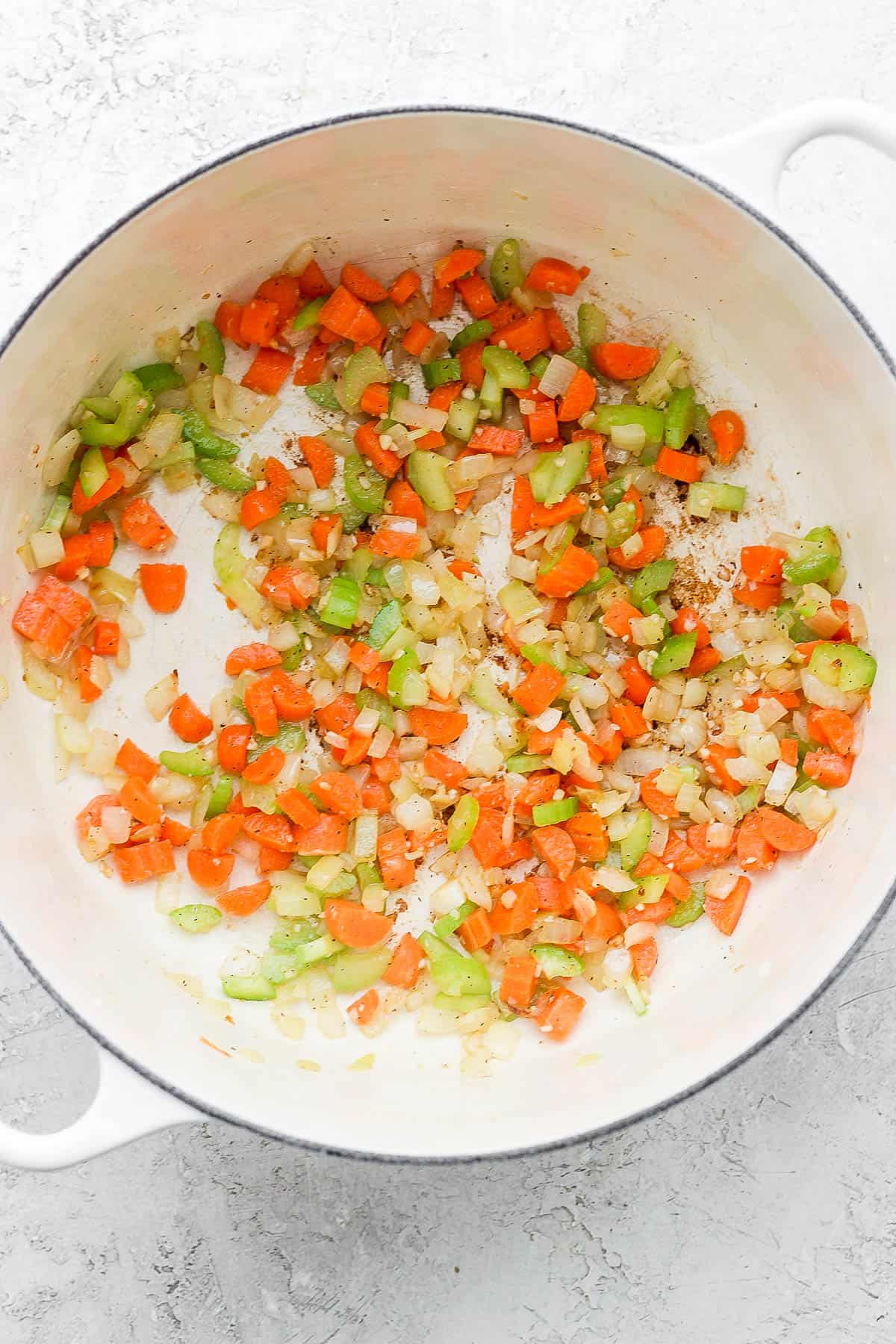 A dutch oven with sautéed onion, garlic, carrots, and celery.