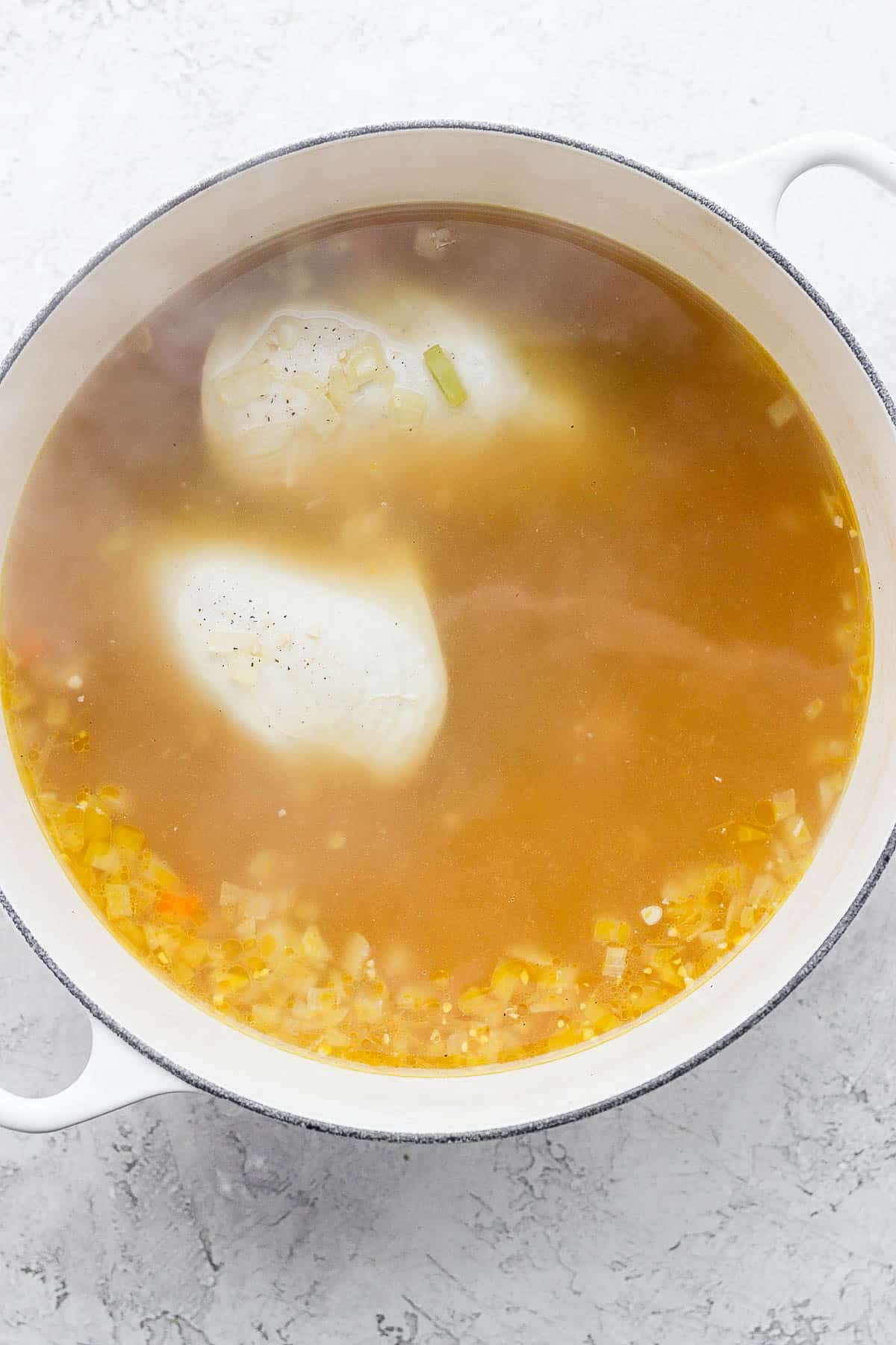 A dutch oven with chicken breasts cooking in the chicken broth.