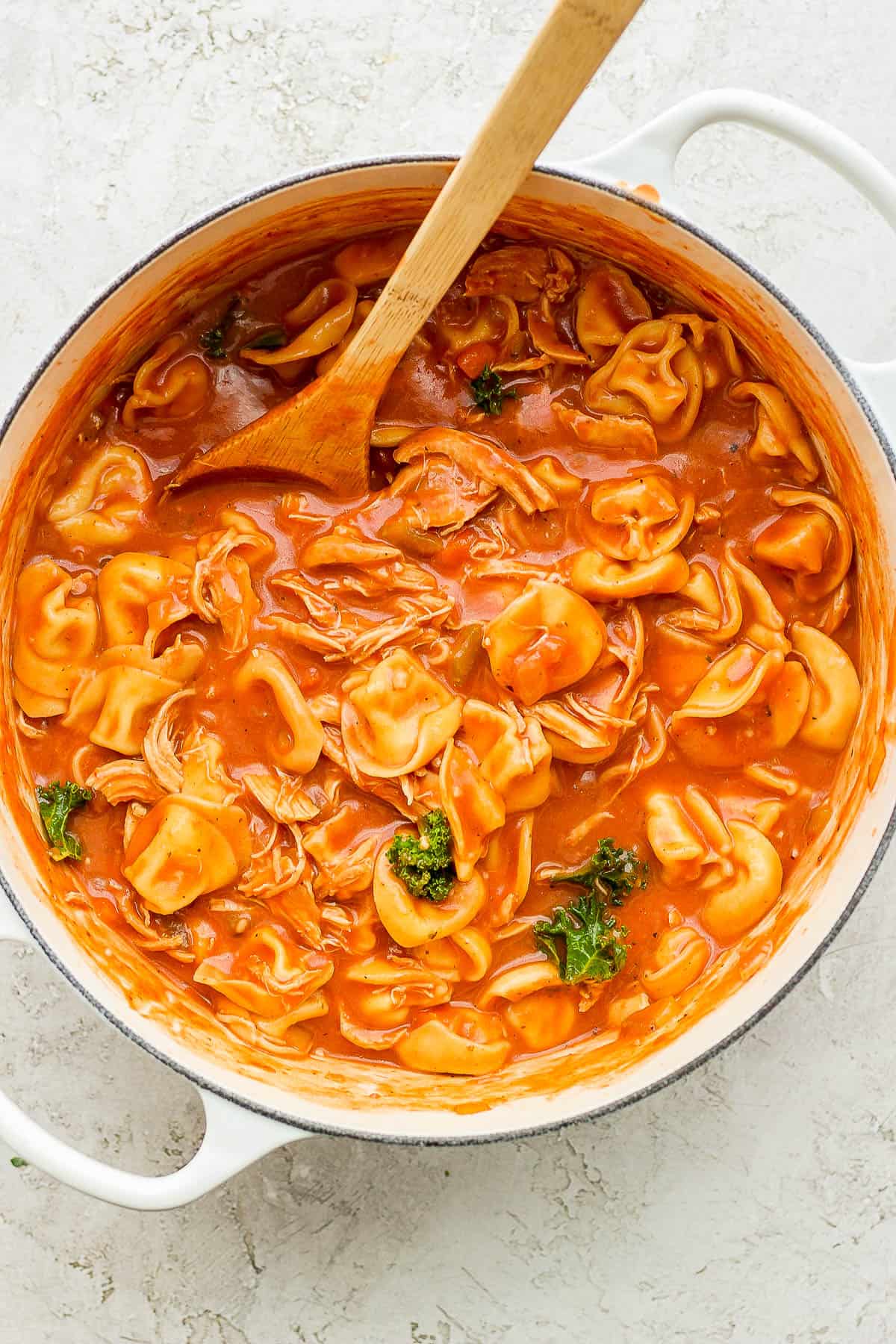 Creamy chicken tortellini soup in a dutch oven with a wooden spoon.