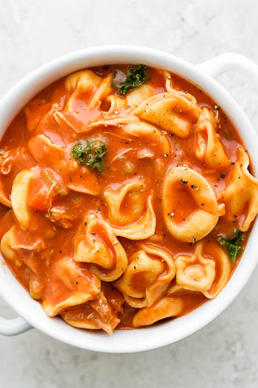 A bowl of creamy chicken tortellini soup with kale.