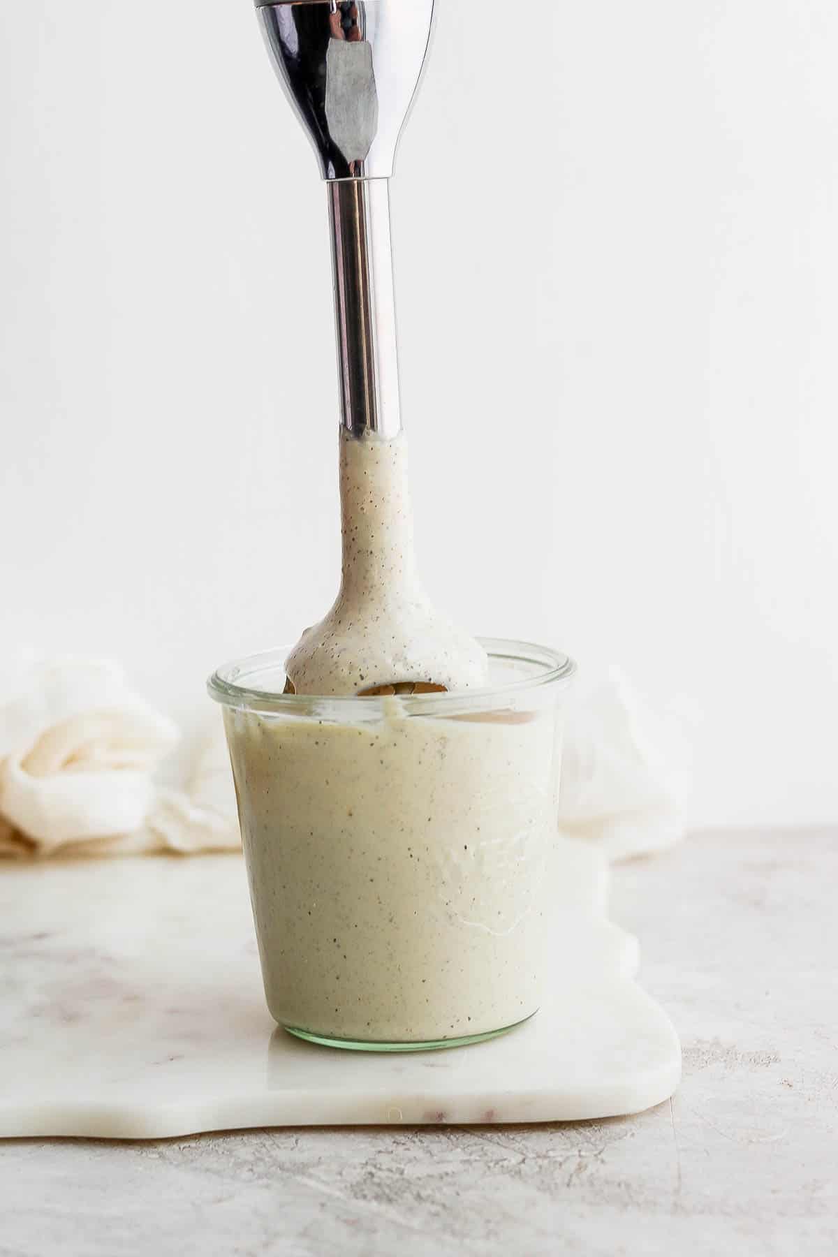 Dairy free caesar dressing in a jar being blended by an immersion blender.