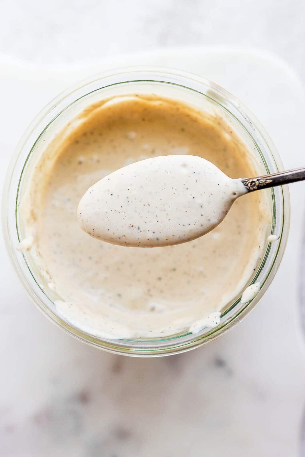 Dairy free caesar dressing in a jar and a spoon is scooping some out.