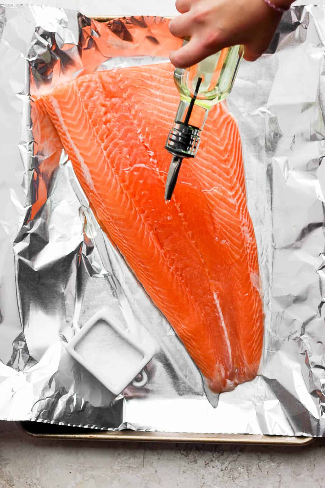 A large salmon fillet on a piece of aluminum foil with olive oil being drizzled on top.