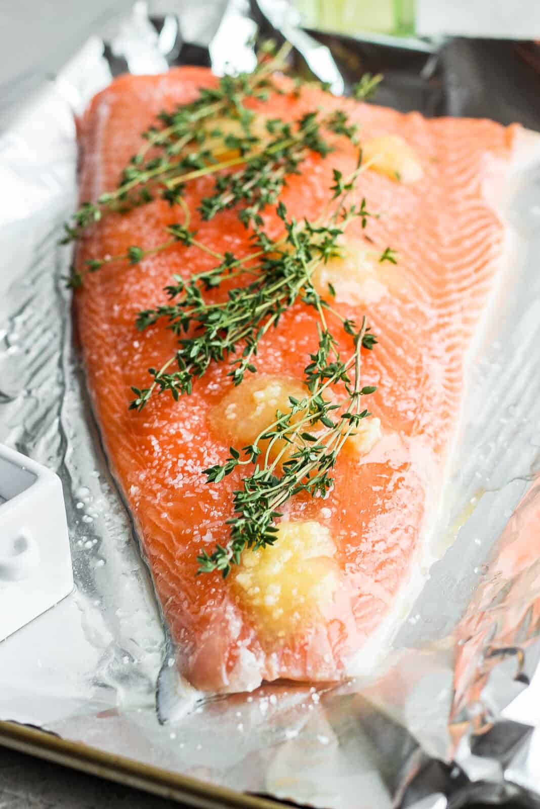 A large salmon fillet with salt, butter, and fresh thyme on top.