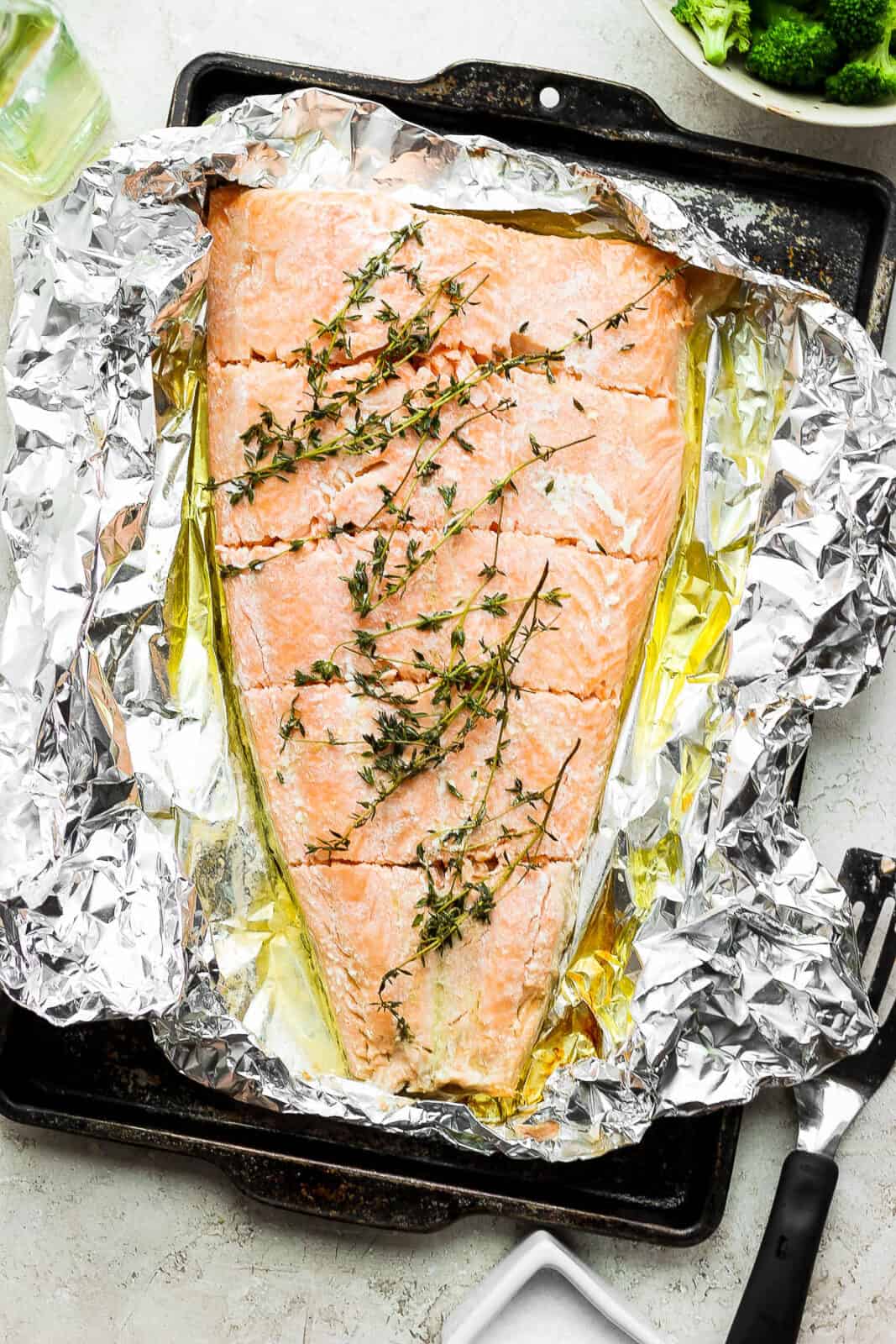 A large baked salmon fillet in foil on a baking sheet.