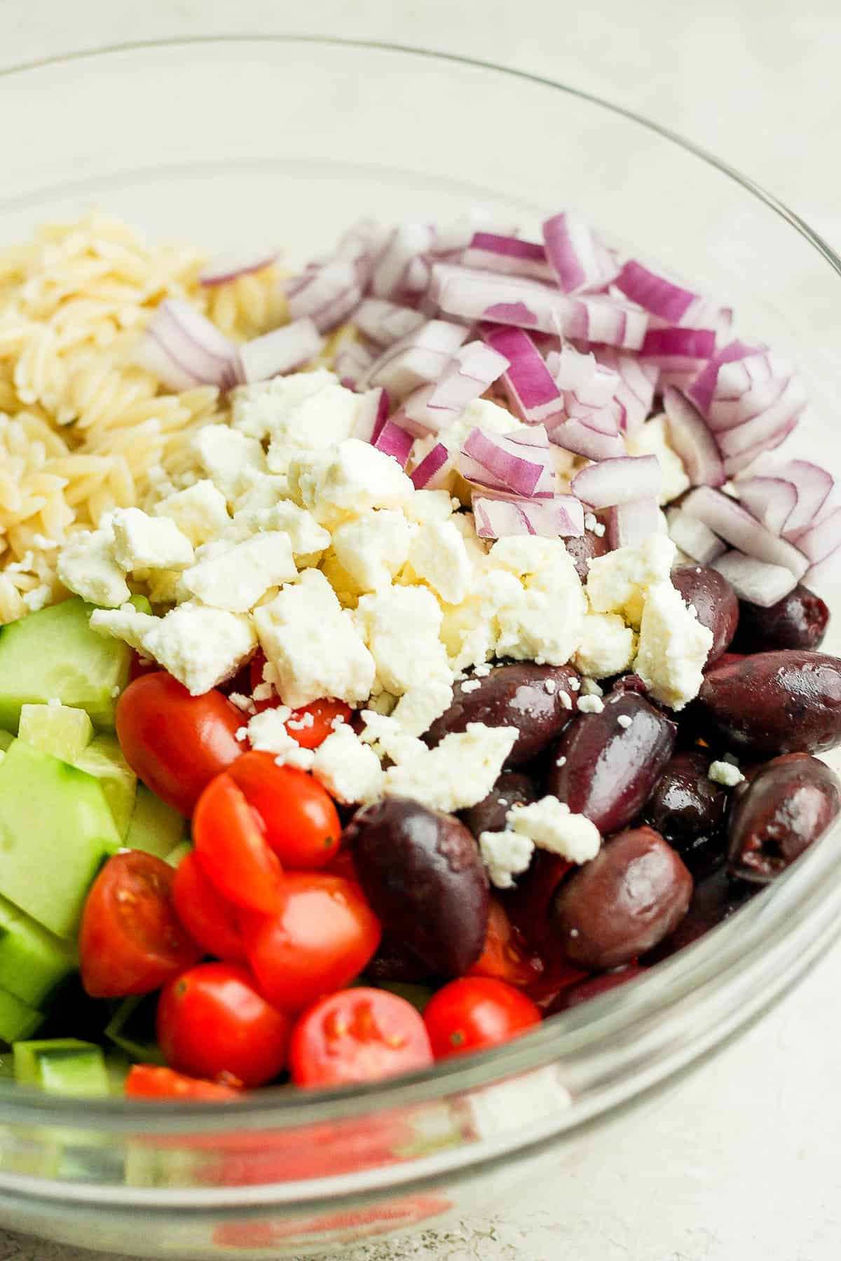 Side angle of ingredients for greek orzo salad in a bowl but not mixed together. 