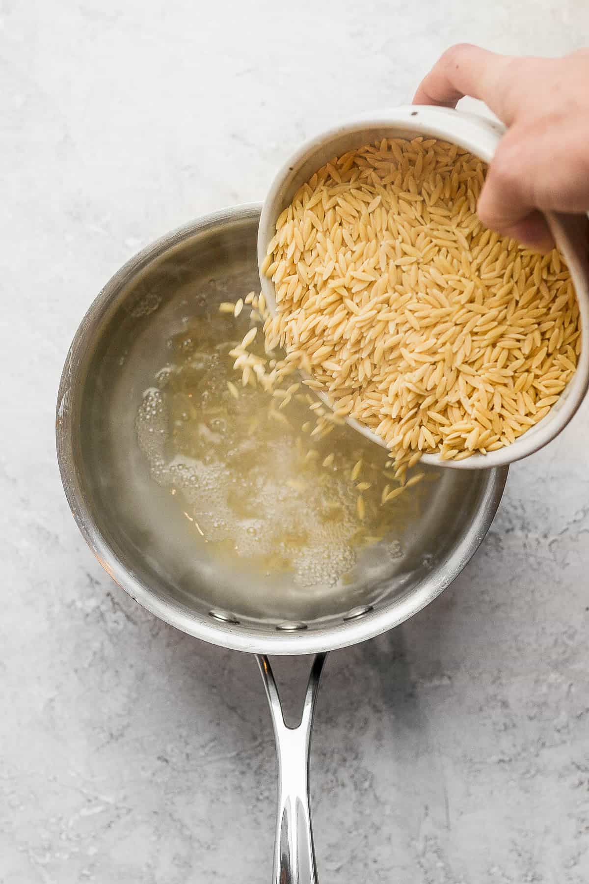 Someone pouring orzo into a pot of boiling water.