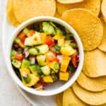 Small bowl of mango pineapple salsa on a plate with chips.