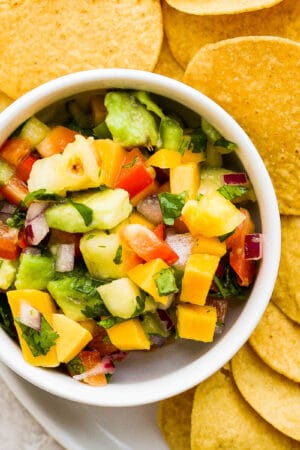 Small bowl of mango pineapple salsa on a plate with chips.