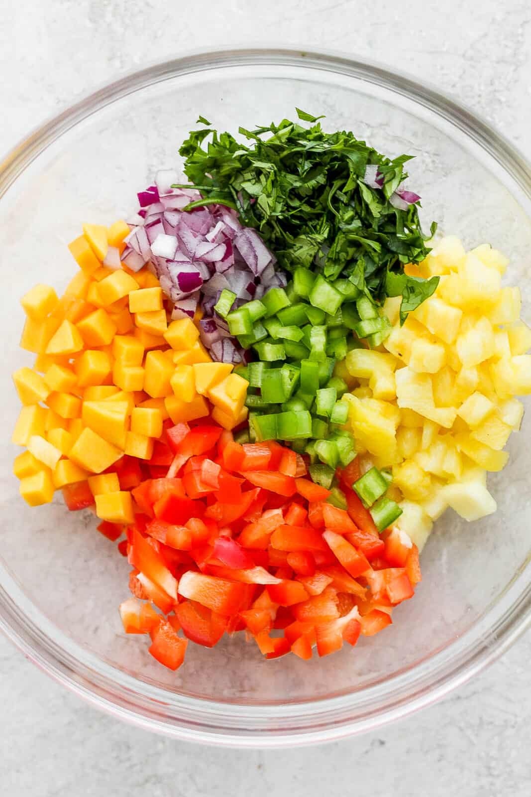 Cut-up pieces of mango, pineapple, red bell pepper, red onion, and cilantro in a mixing bowl.