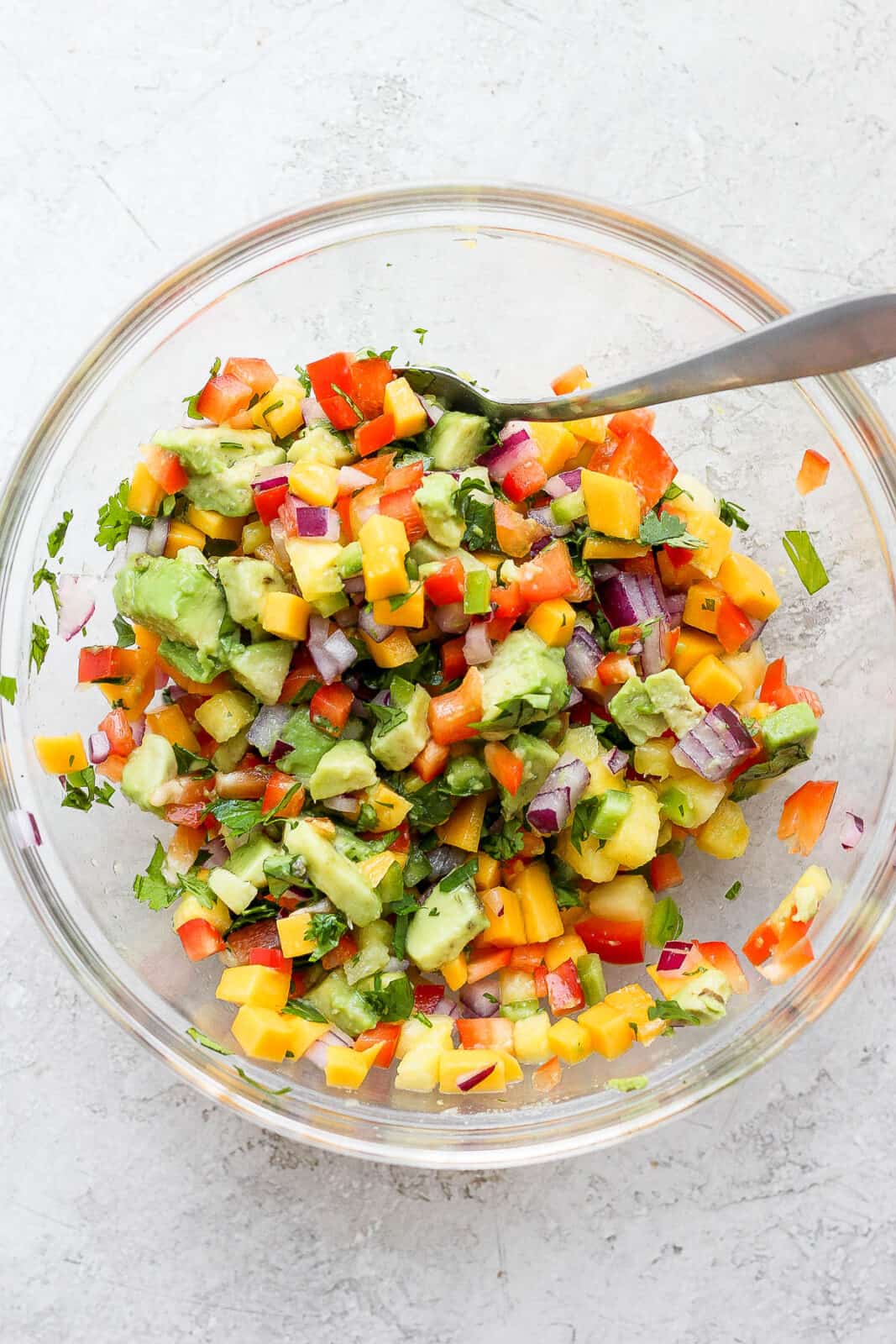 A mixing bowl of mango pineapple salsa with a spoon.