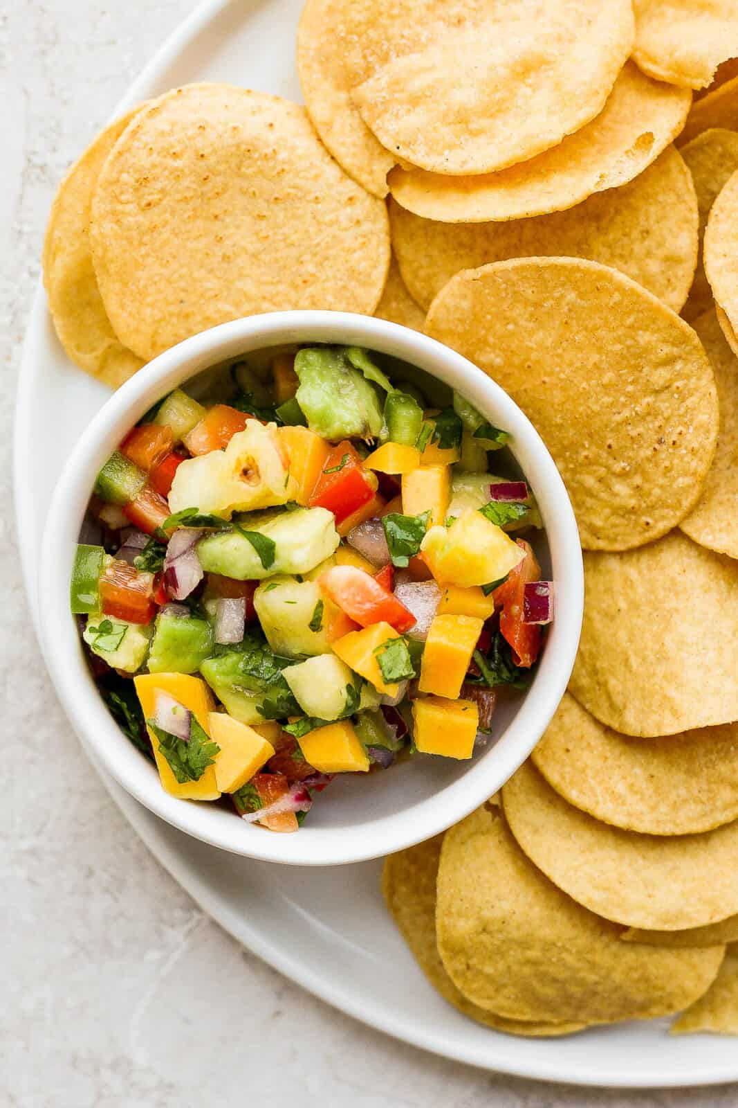 A small dish of mango pineapple salsa on a plate with tortilla chips.
