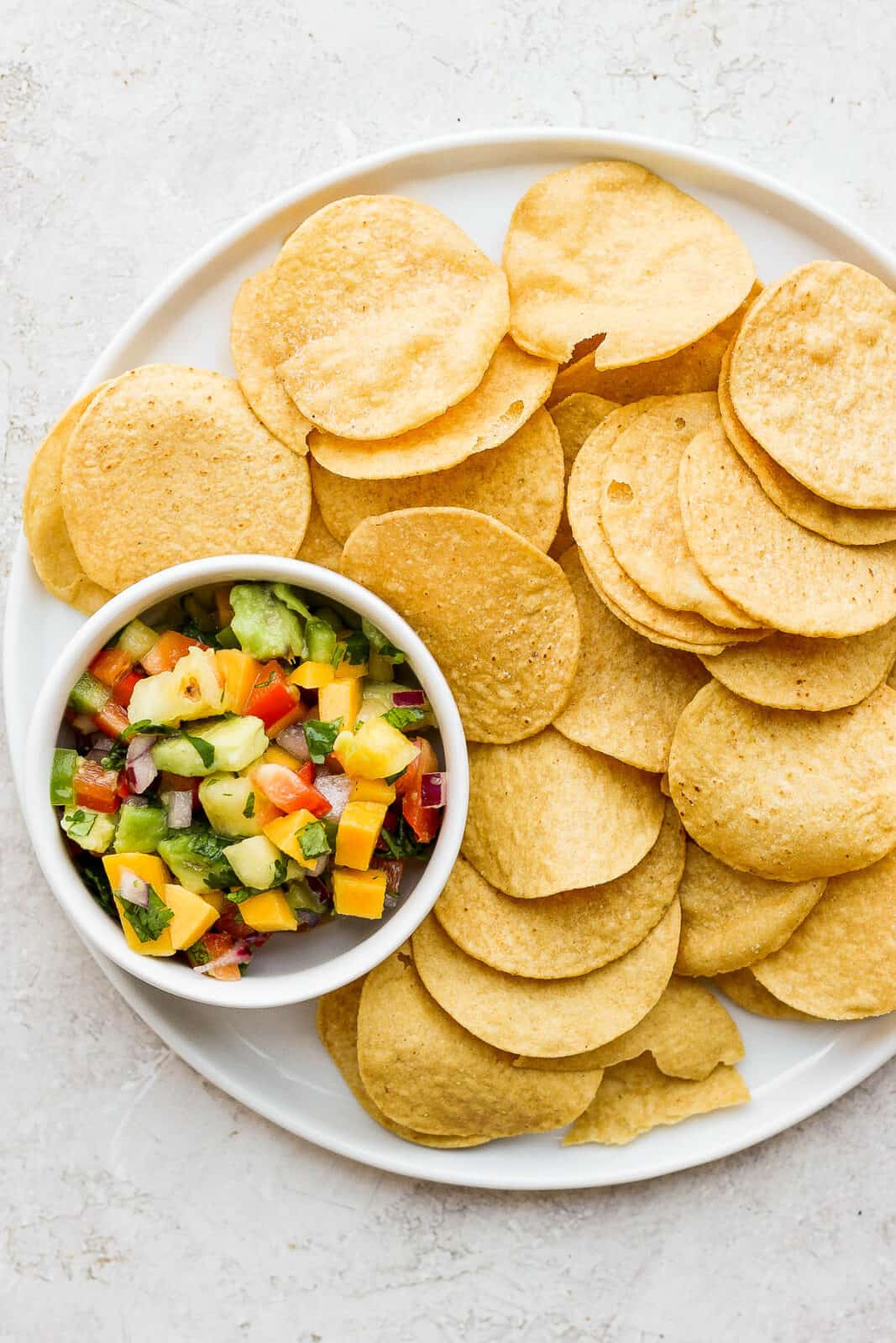 A small dish of fresh mango pineapple salsa with a plate of tortilla chips.