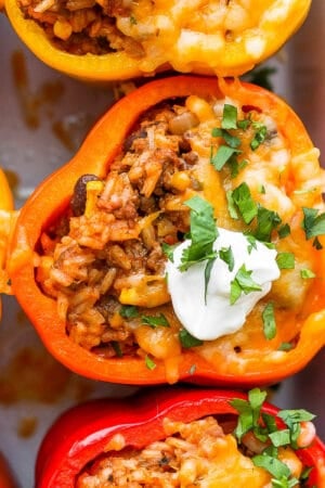 Pan full of mexican stuffed peppers with melted cheese and garnished with sour cream and cilantro,