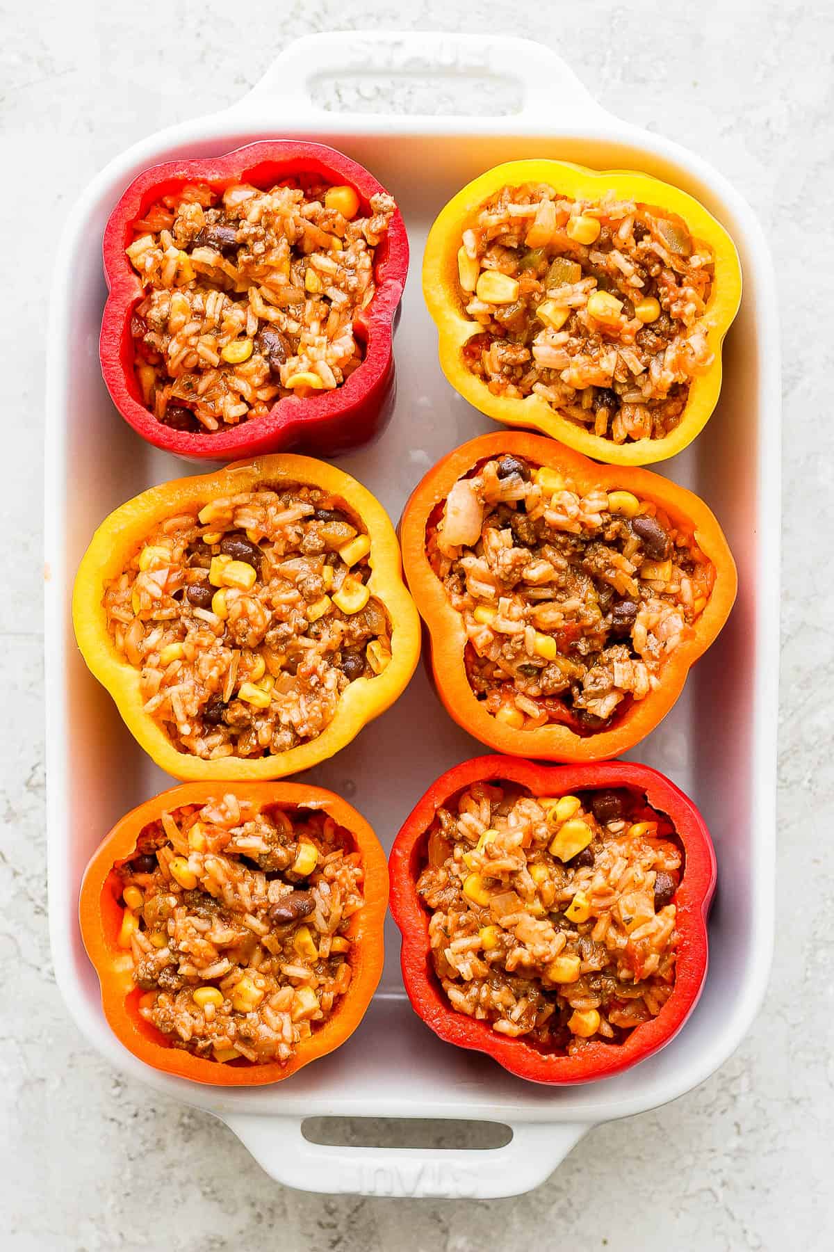 Six hollowed out bell peppers in a baking pan filled with rice.